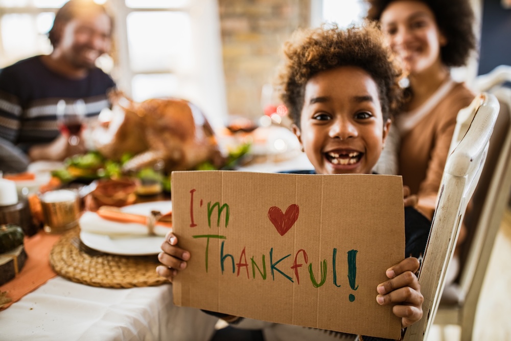 family at table for thanksgiving with little kid holding sign that says I'm Thankful